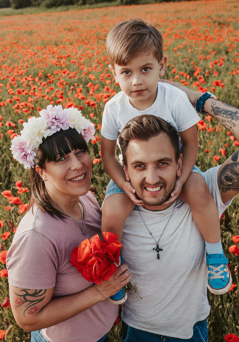 Családi fotózása a piapcsosban. A fotón apa nyakában ül fiú gyermeke, anya virágkoszorút visel a fején