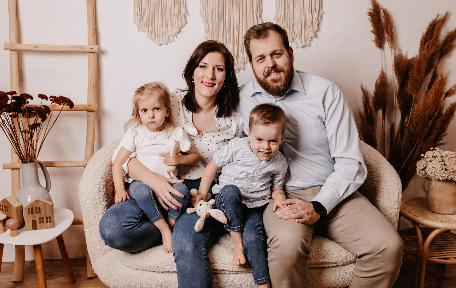 Családi fotózás stúdióban, anya, apa és két gyermekük ül egy kanapén